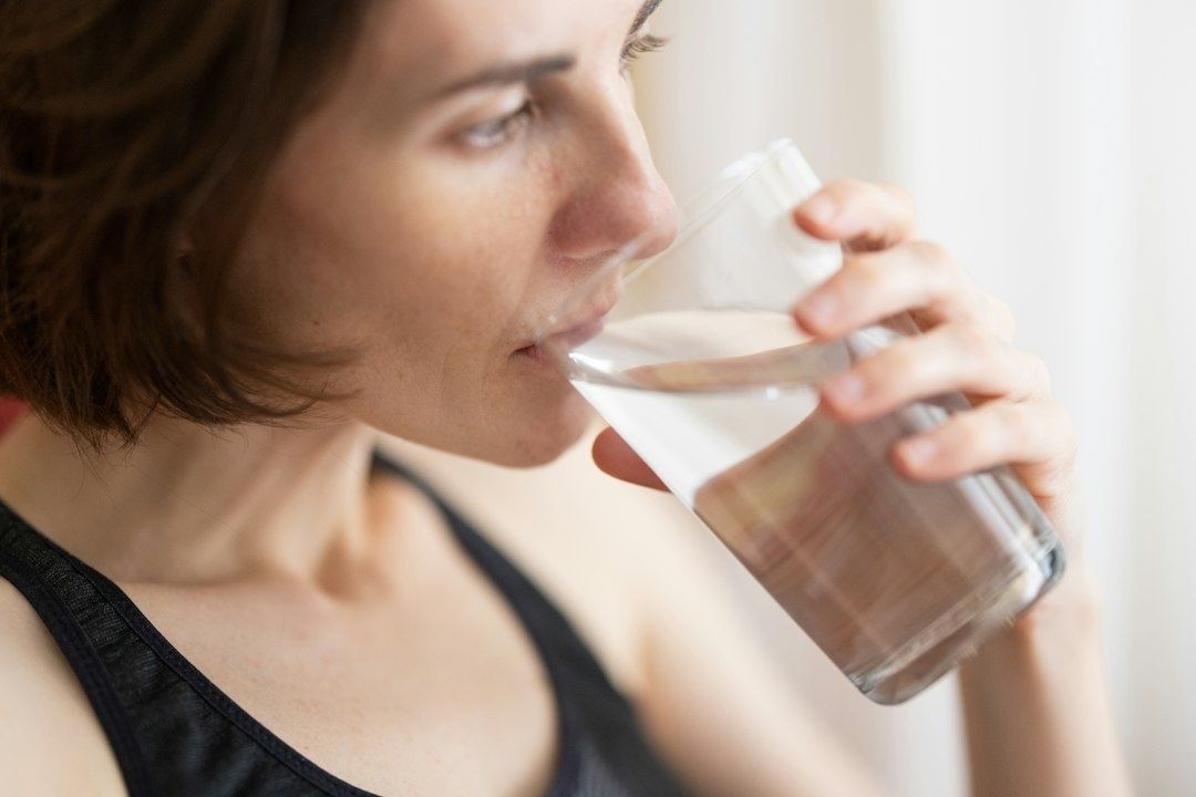 Vrouw drinkt een glas water, passend bij het belang van hydratatie